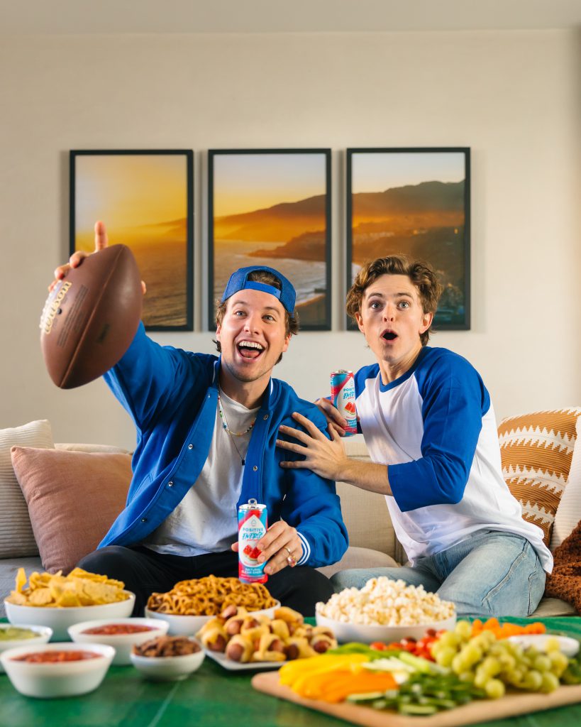 two men watching football with snacks