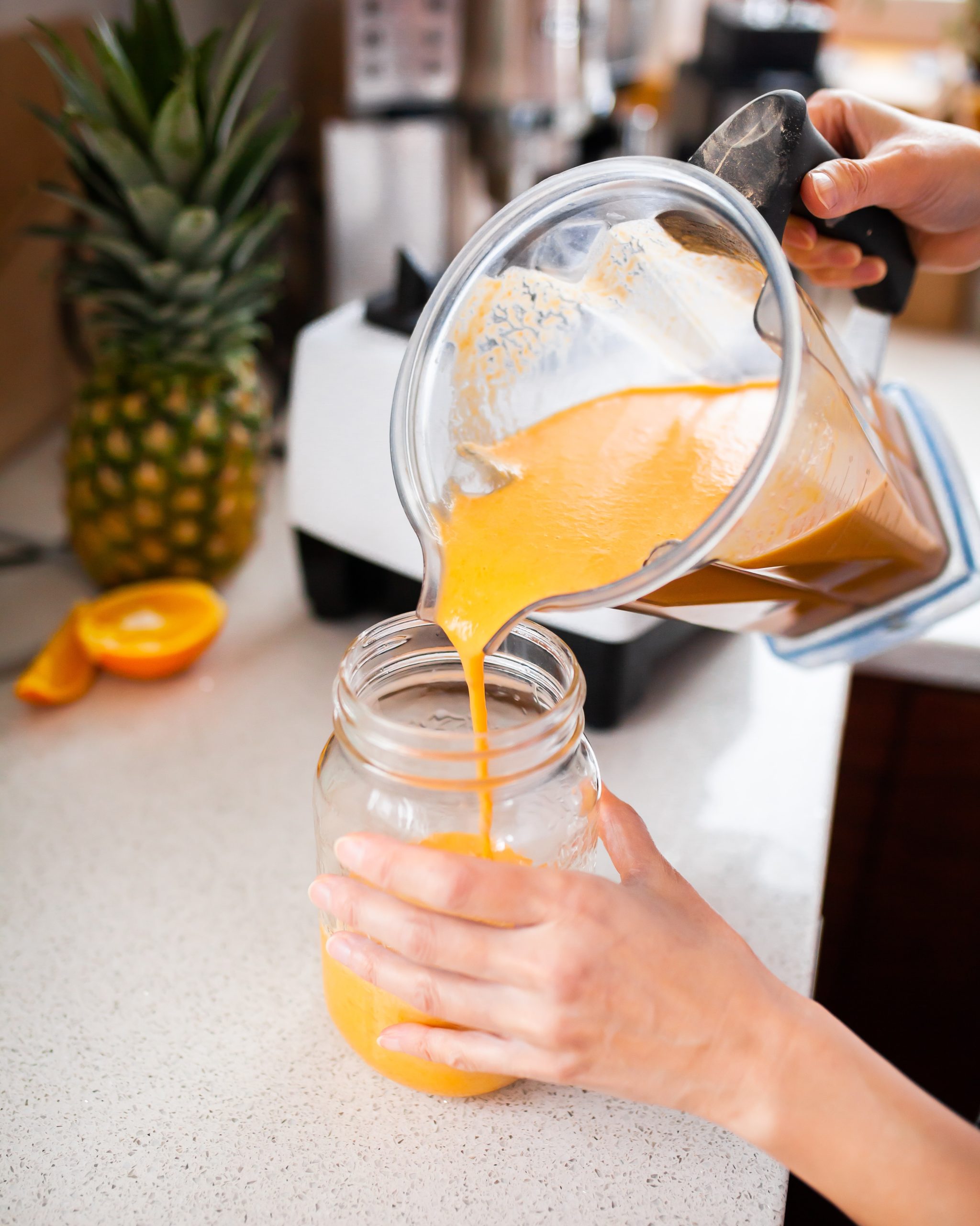 Pineapple orange mango recovery smoothie being poured from a blender into a mason jar