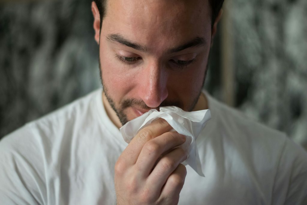 A bearded man covers his mouth while possibly having an allergic reaction.