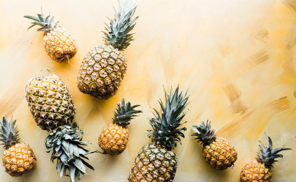 A collection of different sized pineapples, from small to large, on a golden yellow background.