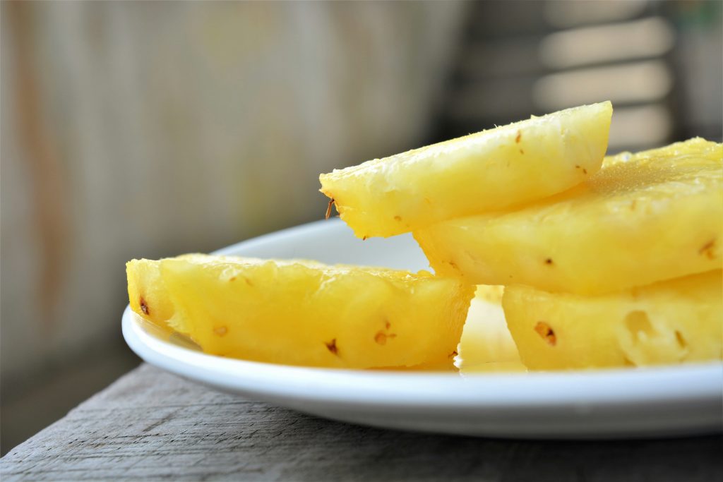 Four slices of pineapple are served on a white plate.