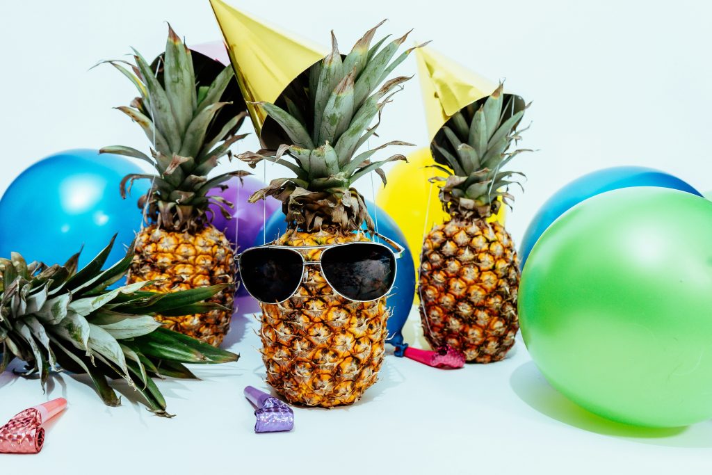 Three pineapples wearing party hats and sunglasses.
